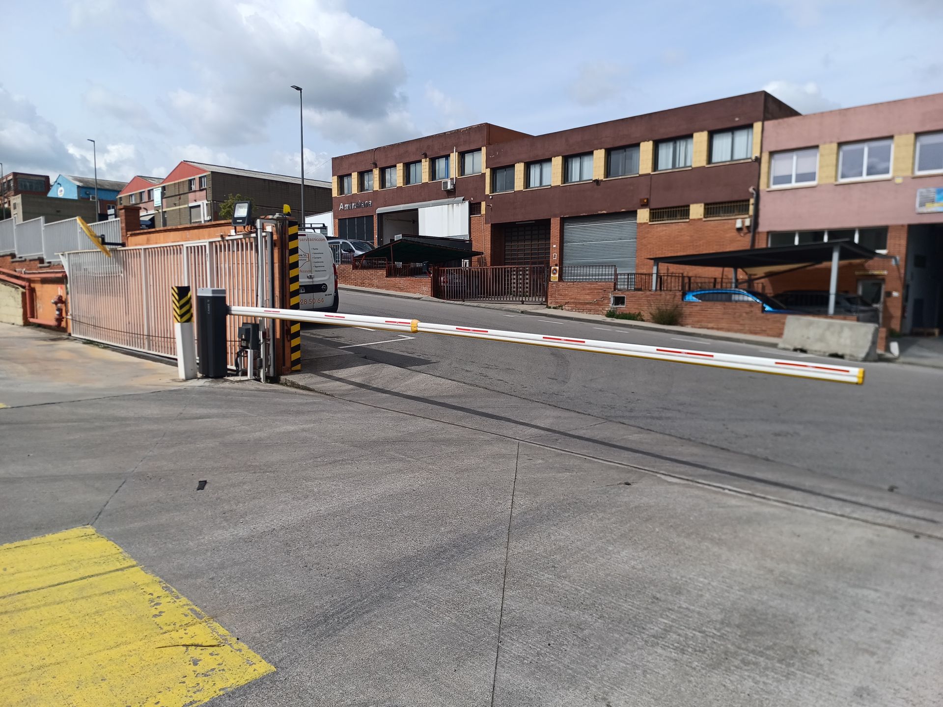 Barrera de acceso en la entrada de un aparcamiento, junto a edificios de ladrillo y vallas naranjas de obra