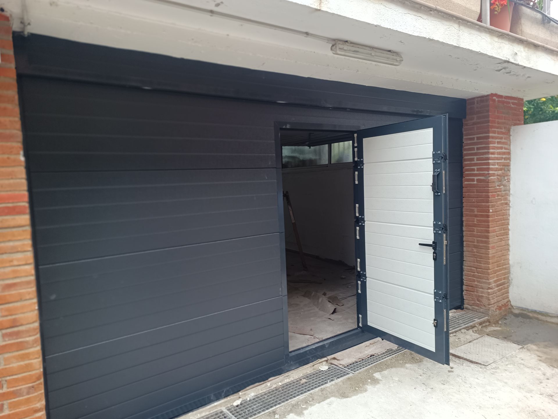 Entrada moderna de tienda, con una puerta de metal negra parcialmente abierta y una pared de ladrillo que enmarca el acceso
