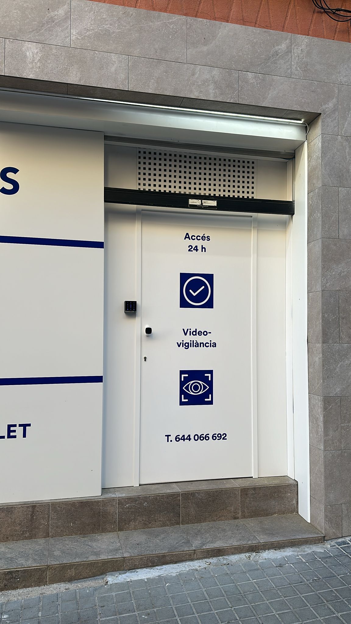 Puerta de un baño accesible bajo un toldo iluminado, señalizada con los símbolos de silla de ruedas y cambiador para bebés.