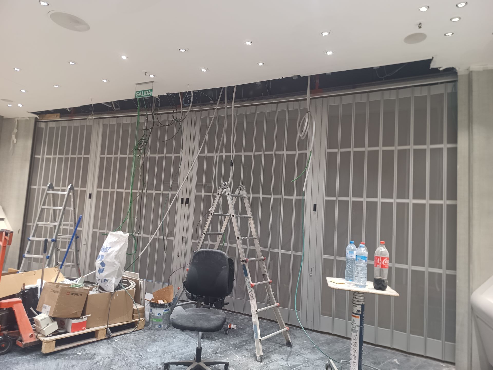Escaparate en obras, con escaleras, herramientas y rejas metálicas de seguridad apiladas en el interior