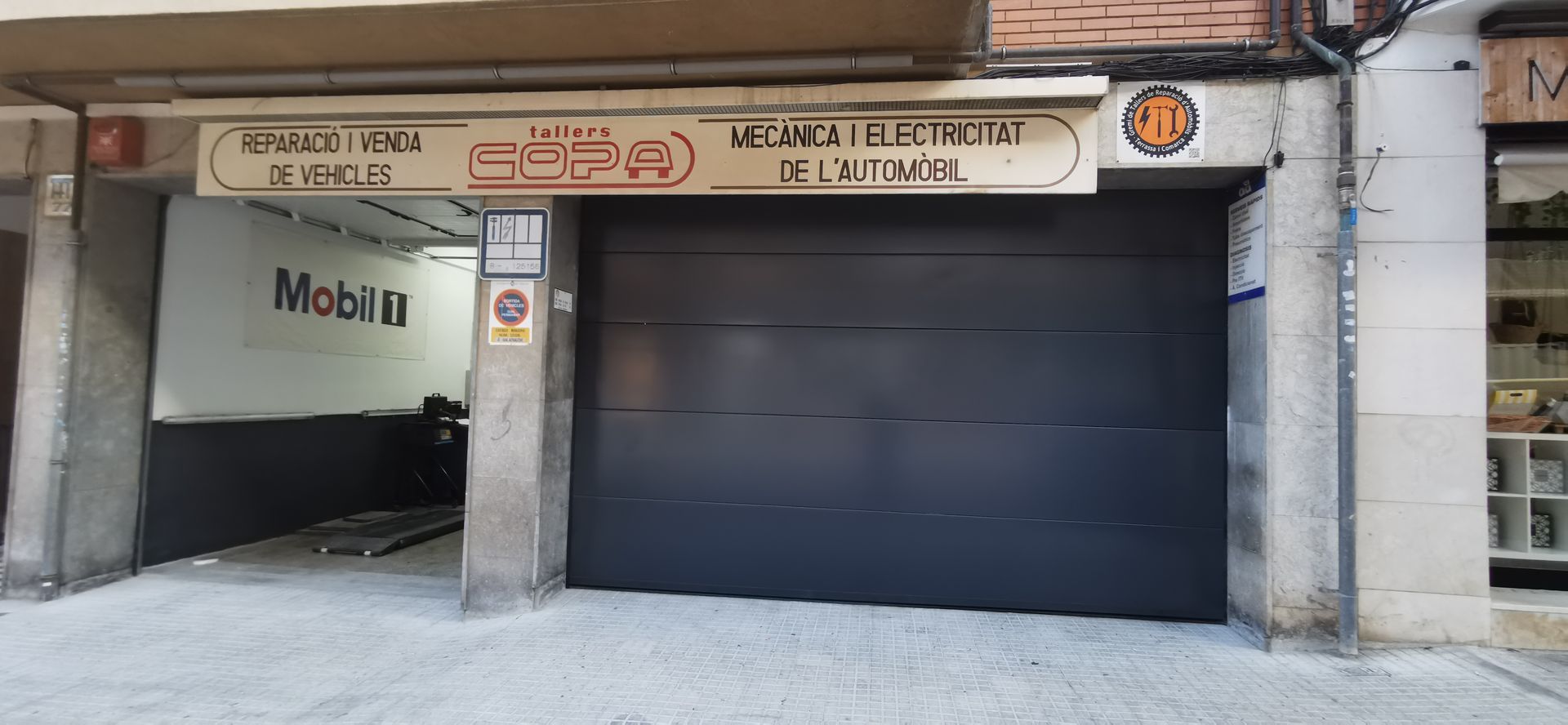 Entrada cerrada de garaje con una puerta negra, pilares de hormigón y un letrero de Mobil arriba.