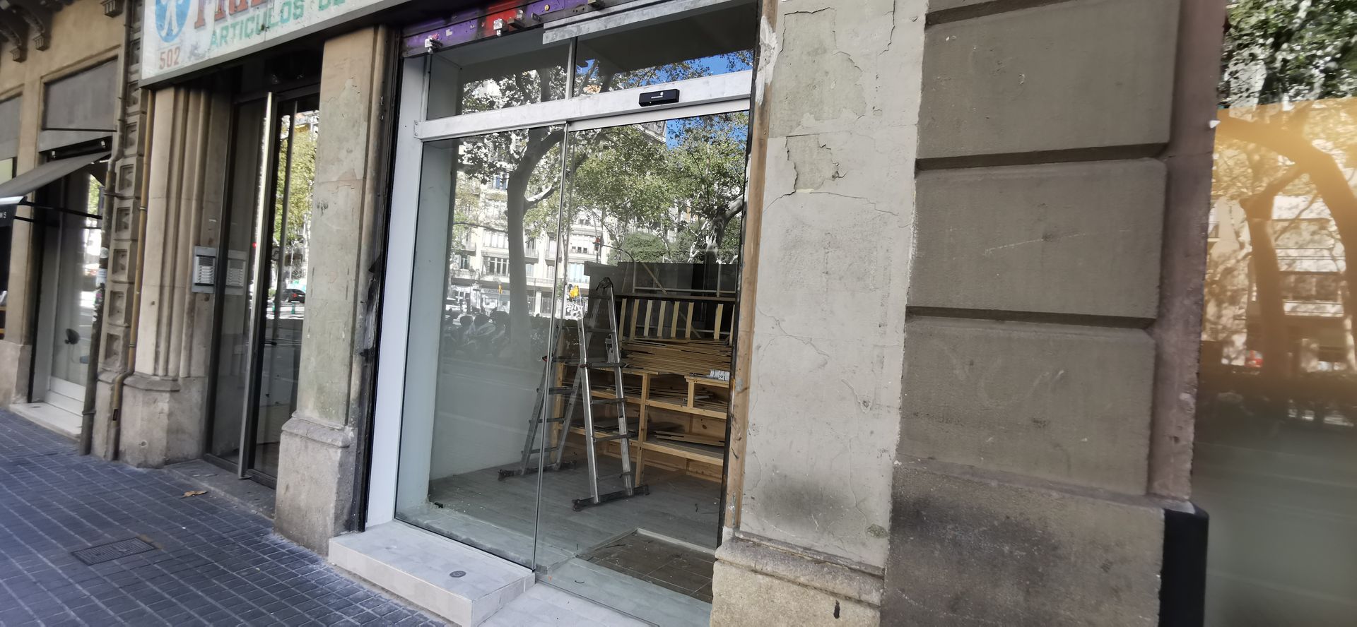 Fachada comercial con puerta y ventanas de cristal, revestimiento de piedra y estanterías de madera visibles en el interior