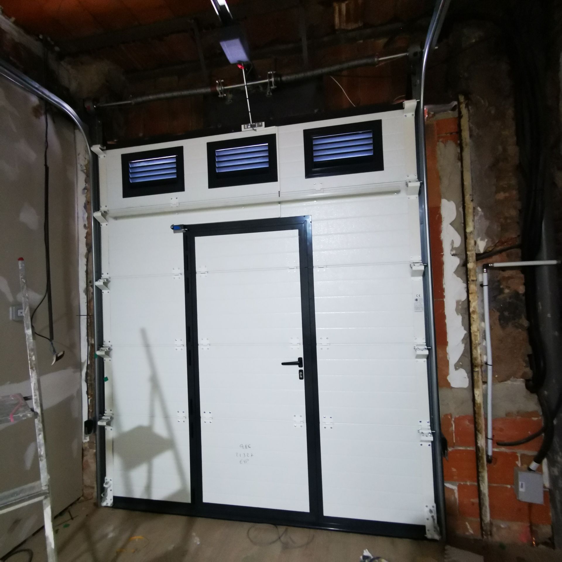 Puerta blanca de estilo garaje con tres ventanas pequeñas en una habitación sin terminar, con las paredes