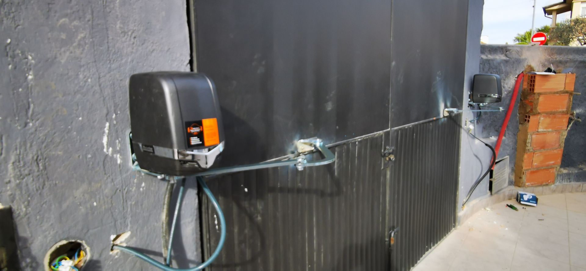 Pared negra con una caja eléctrica instalada, cables expuestos y una manguera azul junto a un pasillo estrecho.