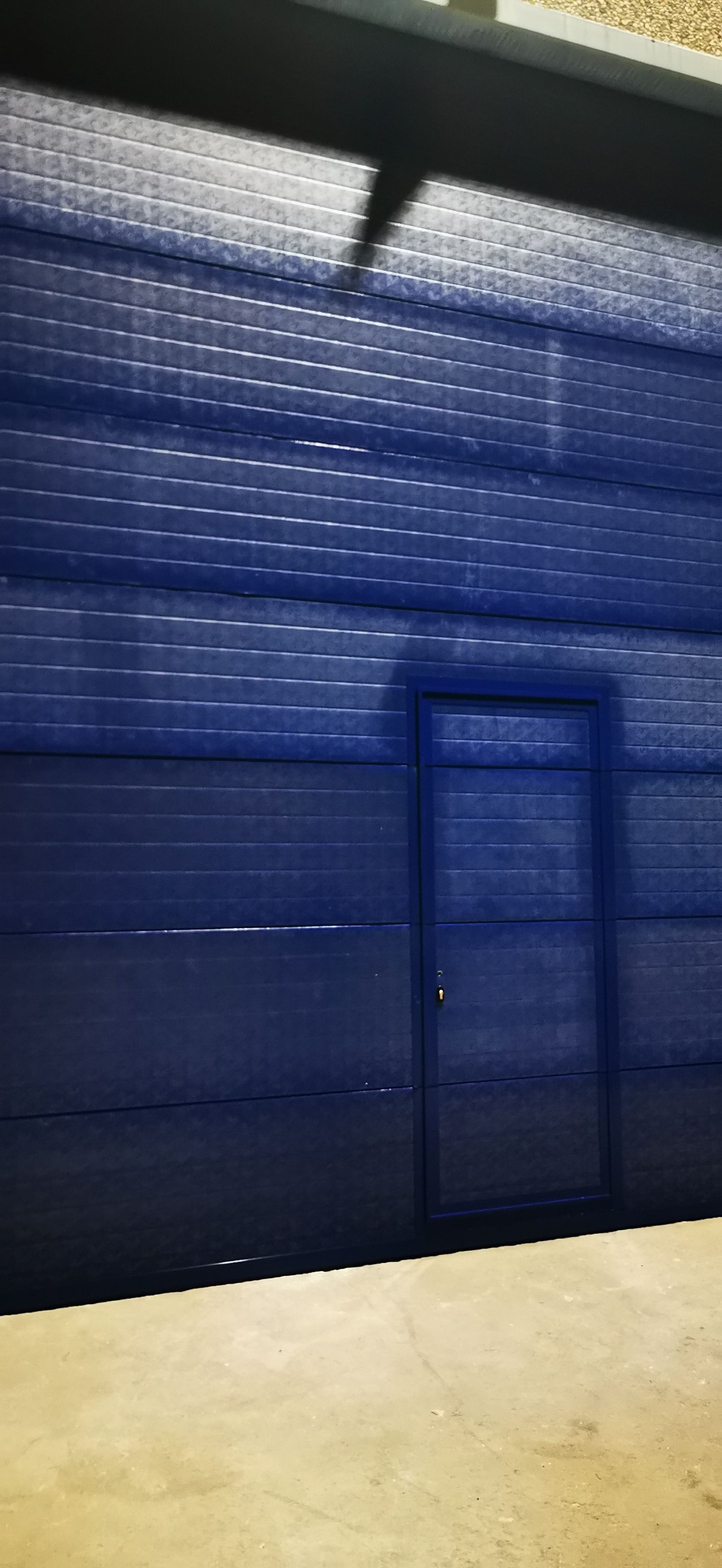 Pared azul de chapa ondulada con una puerta estrecha y un suelo de color claro en el interior