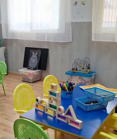 Una habitación con una mesa azul y sillas amarillas llenas de juguetes.