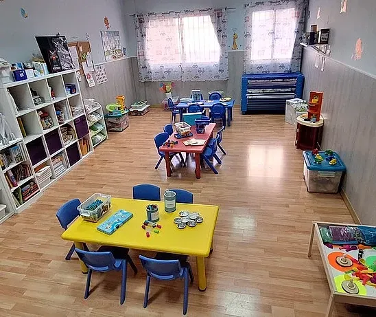 Un aula con mesas y sillas y muchos juguetes.