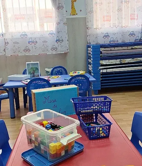 Un aula con una mesa y sillas y una caja de juguetes encima.