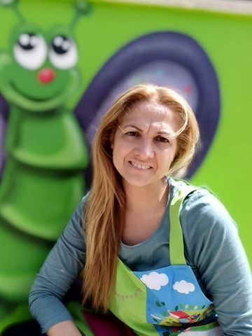 Una mujer que lleva un delantal sonríe delante de una oruga verde.