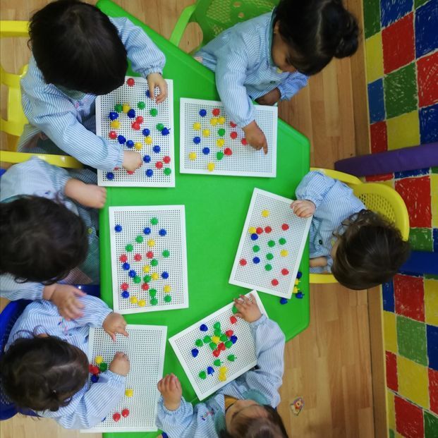 Un grupo de niños está sentado alrededor de una mesa verde jugando con mosaicos.