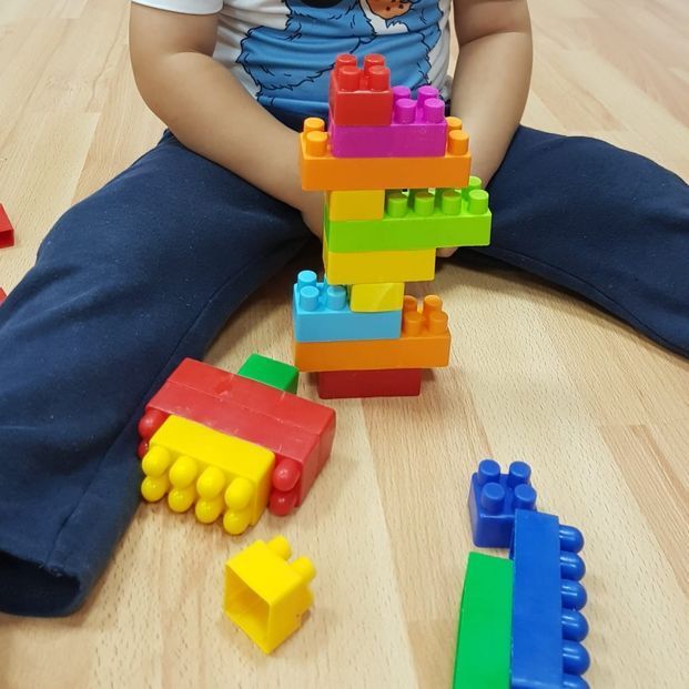 Un niño está sentado en el suelo jugando con bloques Lego de colores.