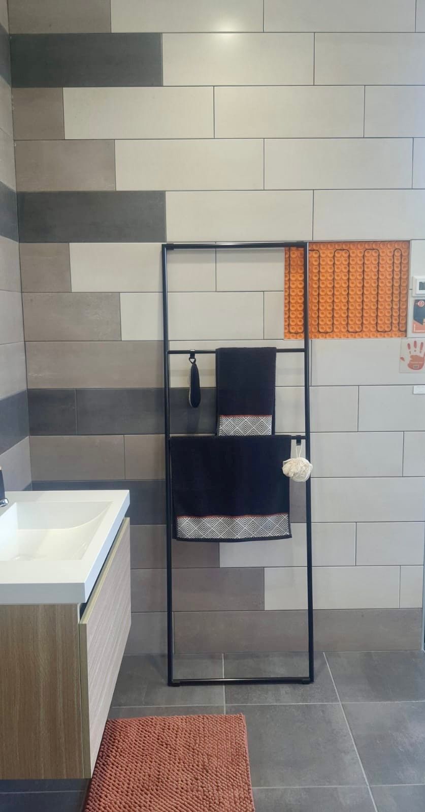 Un meuble-lavabo avec un porte-serviettes contre un mur carrelé de briques grises et blanches