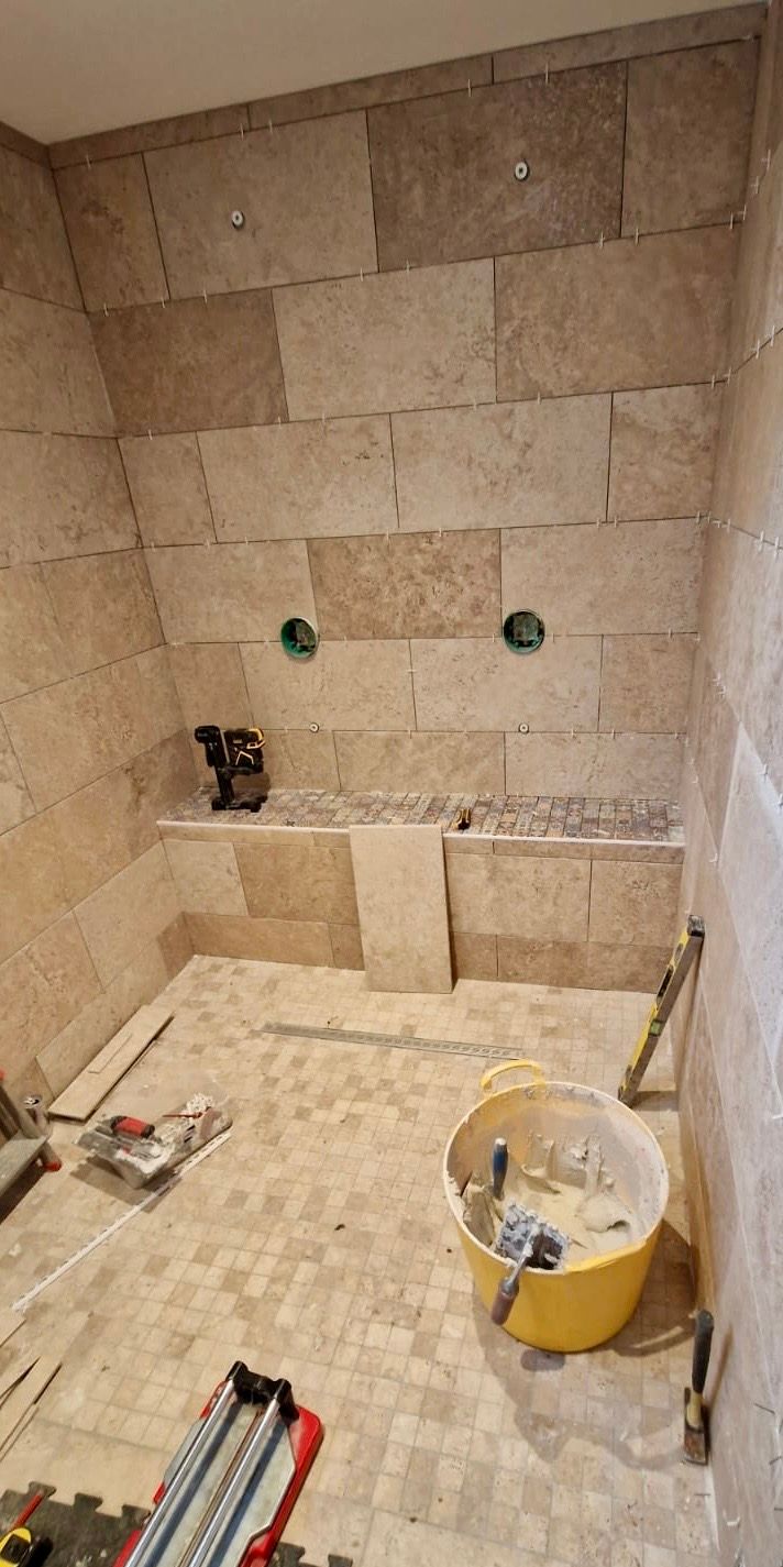Une douche en construction avec des carreaux muraux en pierre beige, un banc intégré et des outils au sol