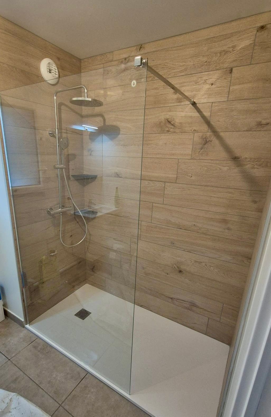 Une douche à l'italienne avec une paroi en verre et des murs carrelés imitation bois clair