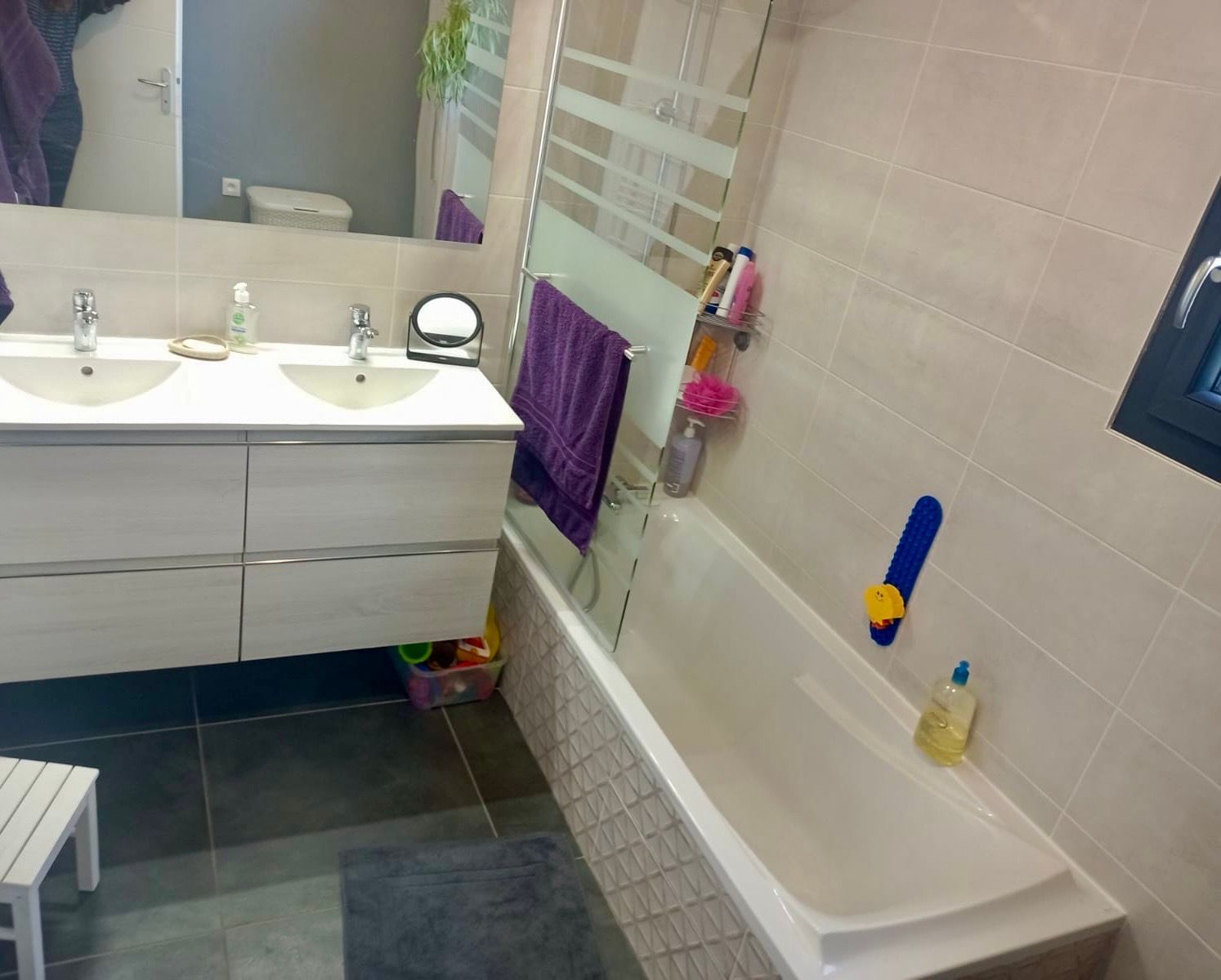 Salle de bains avec une double vasque, une baignoire avec paroi de verre et des murs carrelés