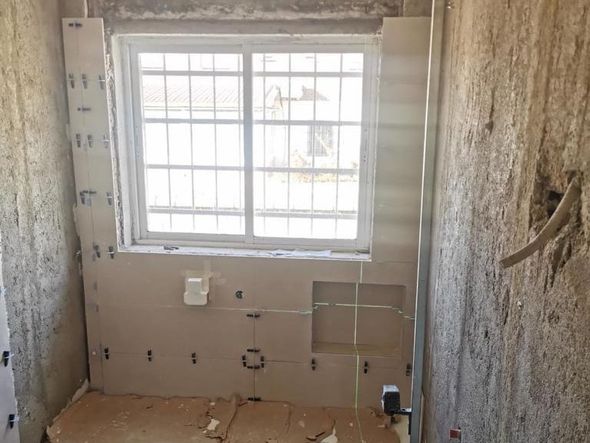 Baño en construcción con ventana, cableado a la vista y paredes sin terminar.