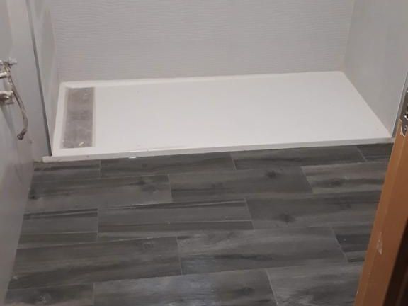 Baño con suelo de baldosas imitación madera gris y lavabo de ducha blanco. Se ha colocado una pequeña sección de baldosas.