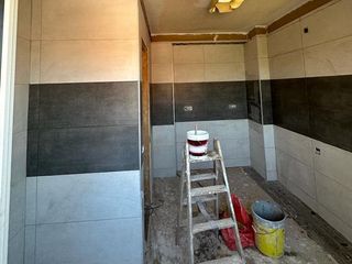 Baño en construcción con paredes de azulejos blancos y gris oscuro, escalera y latas de pintura.