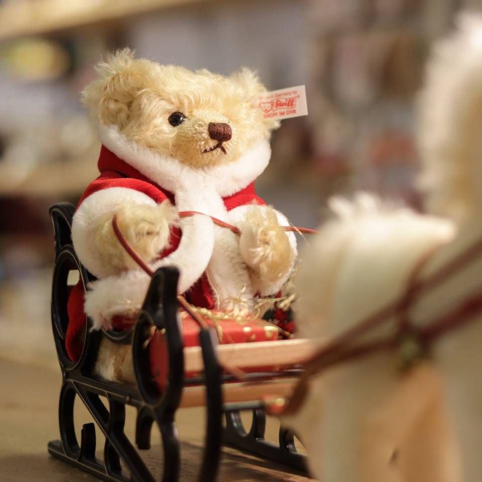 Cheval en peluche blanc avec un bridon et une clochette rouges, montré en gros plan sur un fond flou.