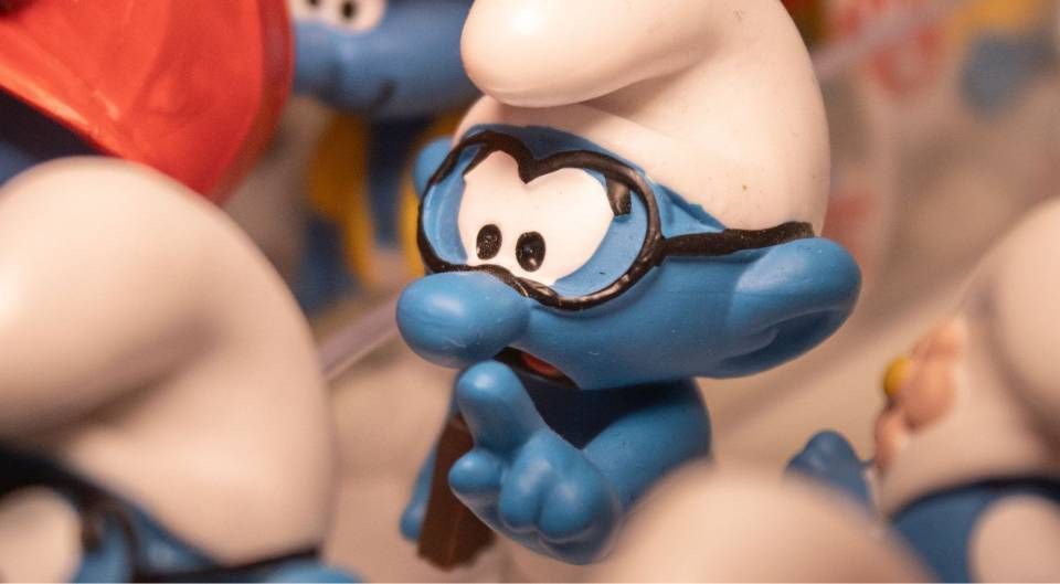 Gros plan sur une figurine de Schtroumpf bleu à lunettes rouges parmi d'autres figurines de Schtroumpfs