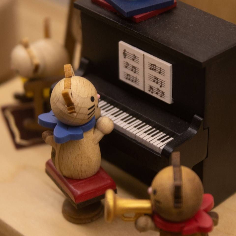 Des figurines en bois jouent du piano, l'une avec une écharpe bleue.