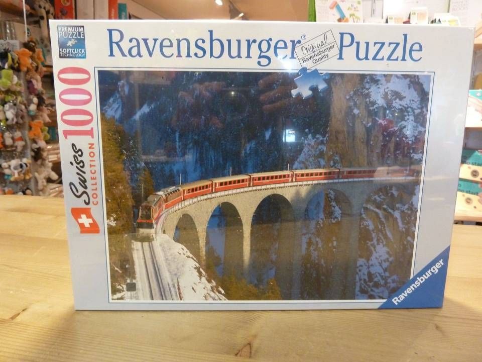 Boîte de puzzle Ravensburger de 1000 pièces représentant un train rouge traversant un pont en arc au-dessus d'une rivière