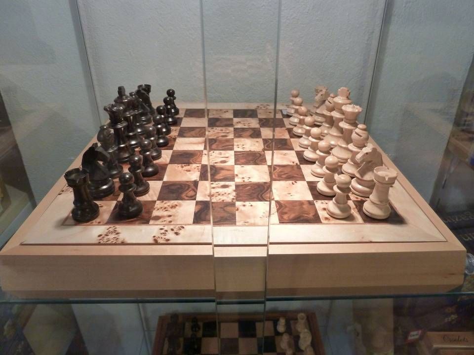 Échiquier en bois avec pièces noires et blanches disposé dans une vitrine.