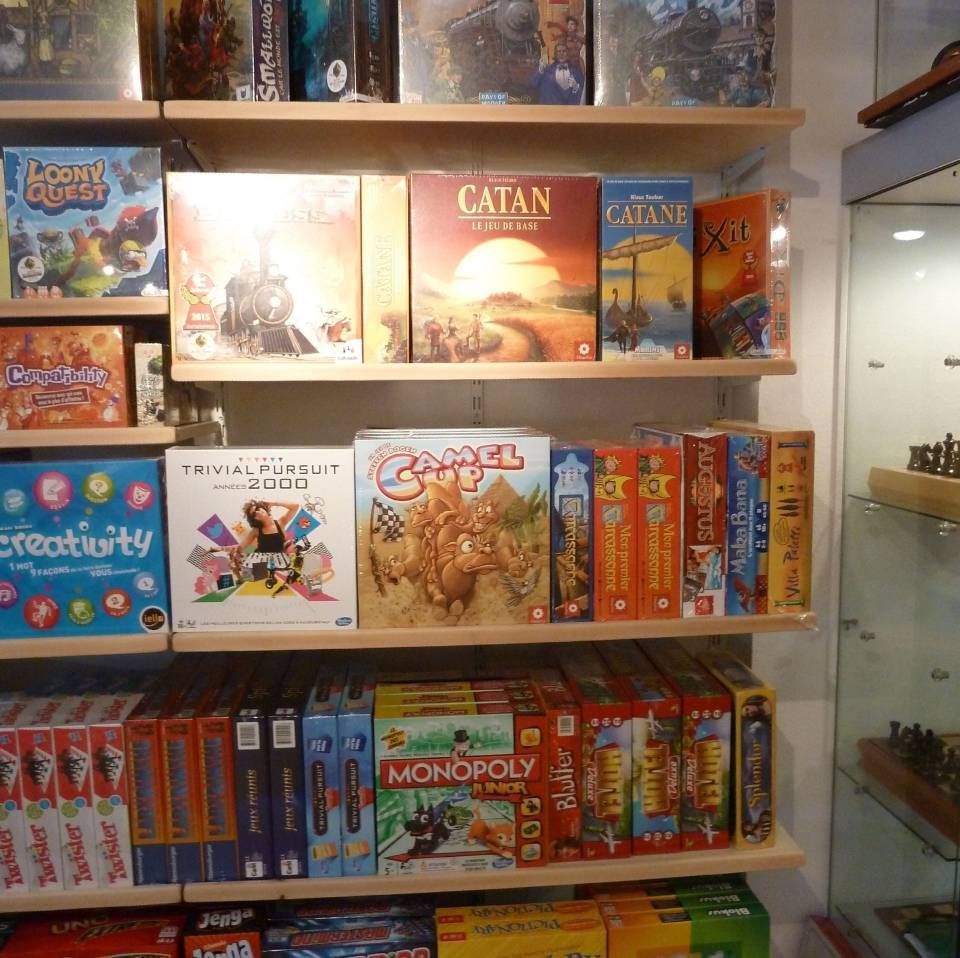 Des étagères remplies de jeux de société colorés dans un magasin, notamment Catan et Monopoly.