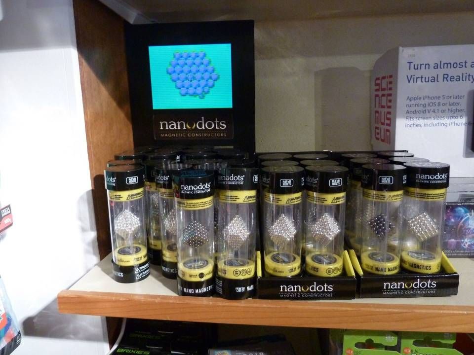 Étagère présentant les produits NanoDots dans des bocaux noirs, avec un panneau d'affichage bleu derrière.