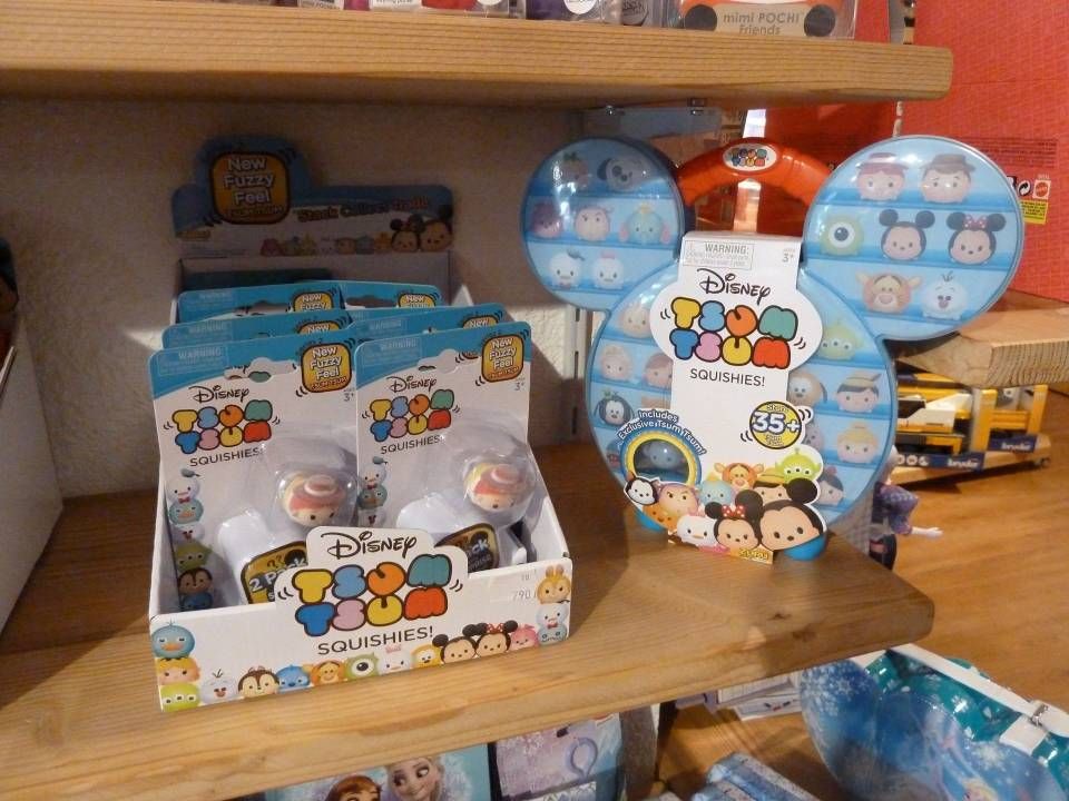 Présentoir de produits Disney Tsum Tsum sur des étagères en bois, avec emballages bleus et blancs et boîtes rondes à l'effigie des personnages.