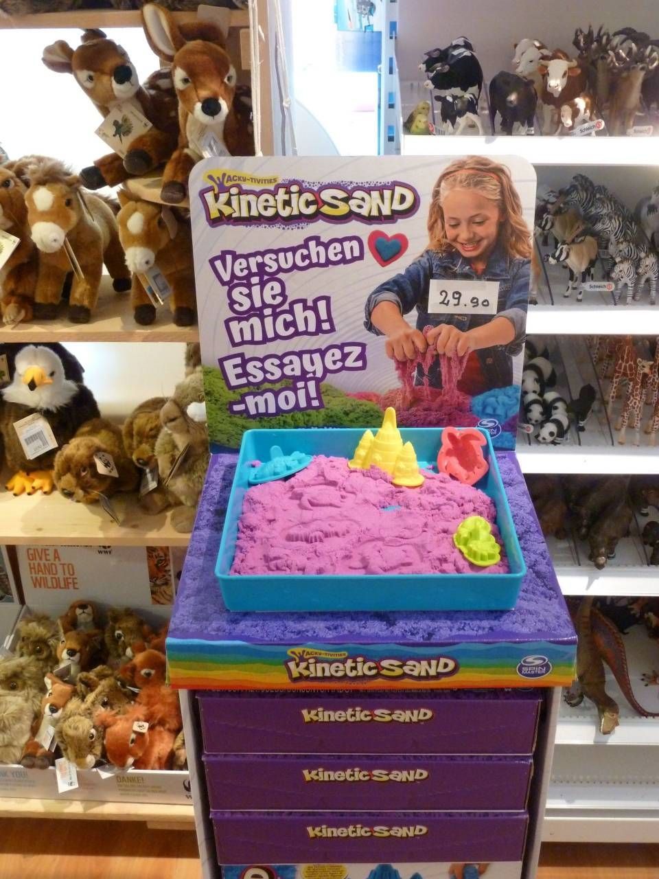 Présentoir de sable cinétique avec des moules à sable colorés et une pancarte « soldes » dans un rayon de magasin de jouets.