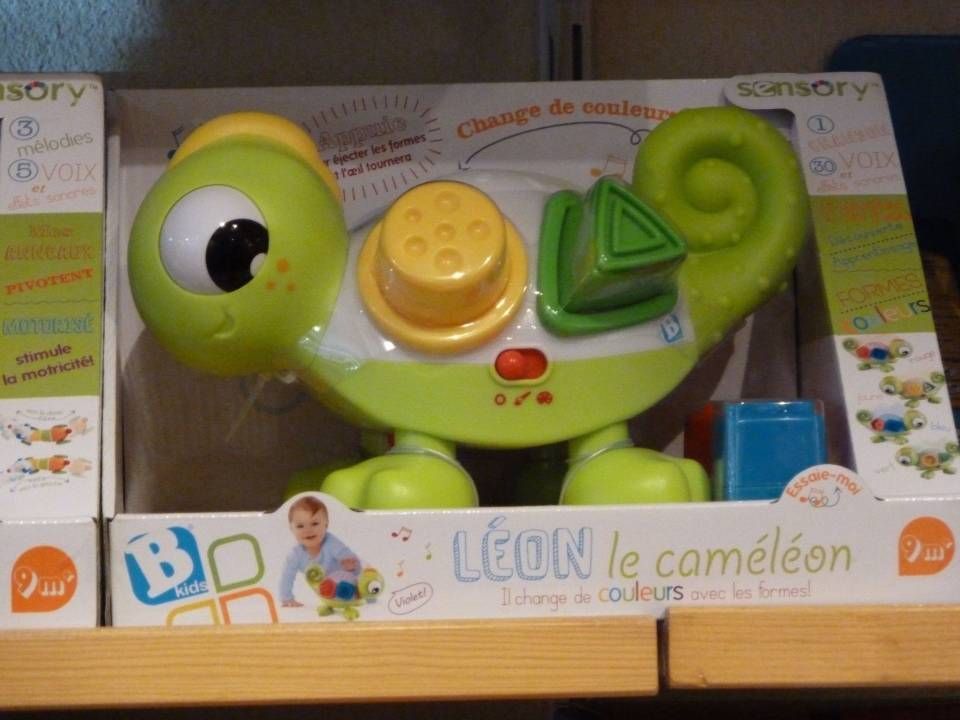 Caméléon jouet vert avec des boutons colorés, dans sa boîte, sur une étagère de magasin