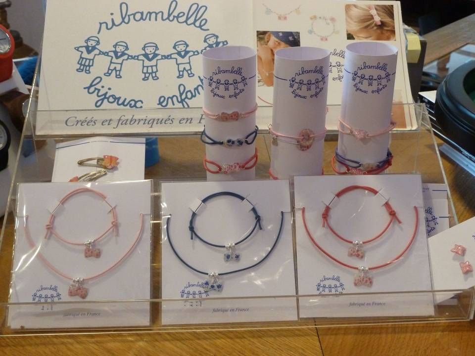 Présentation de bracelets artisanaux sur des cartes, avec une petite pancarte et des tubes en papier pastel en arrière-plan.