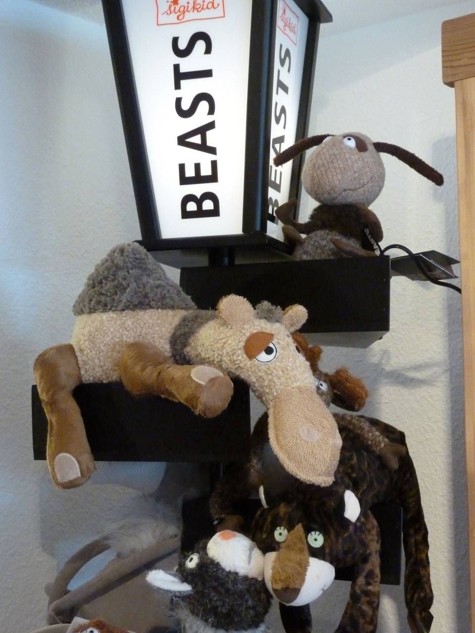 Des peluches empilées sur des étagères noires à côté d'une lampe étiquetée « BÊTES ».