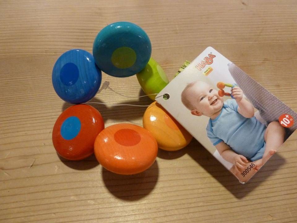Hochet coloré pour bébé avec des anneaux bleus, rouges, oranges et verts sur une surface en bois, accompagné d'une carte photo de bébé