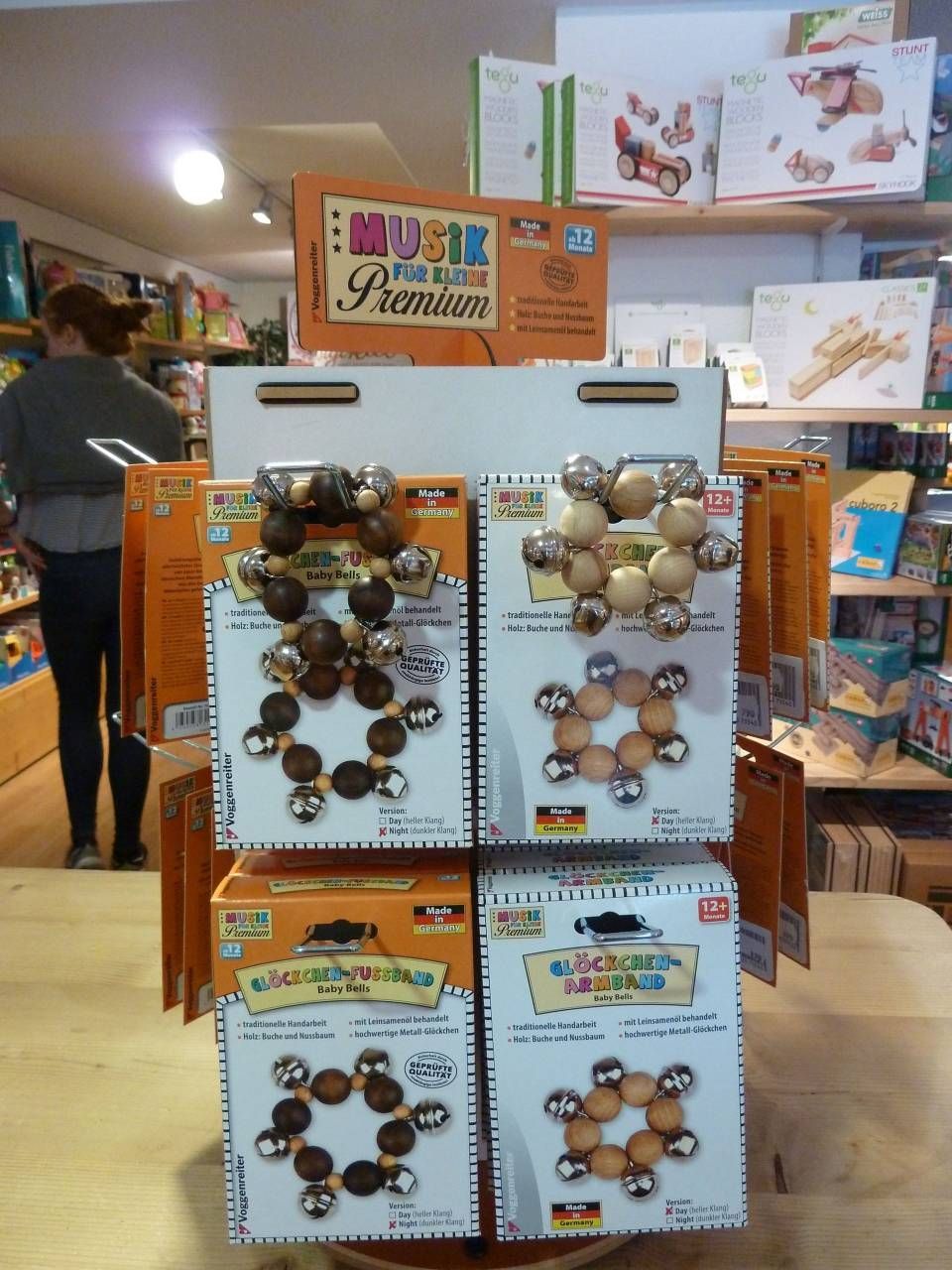Présentoir à bijoux avec bracelets de perles dans une boutique, avec des étagères et un client en arrière-plan