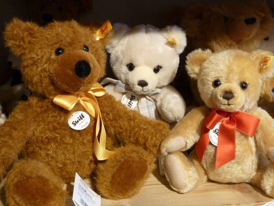 Trois ours en peluche exposés : un brun, un blanc et un beige, chacun orné d'un nœud en ruban.