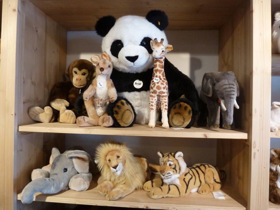 Des animaux en peluche sur des étagères en bois, notamment un panda, une girafe, un éléphant, un lion, un tigre et des peluches d'éléphant.