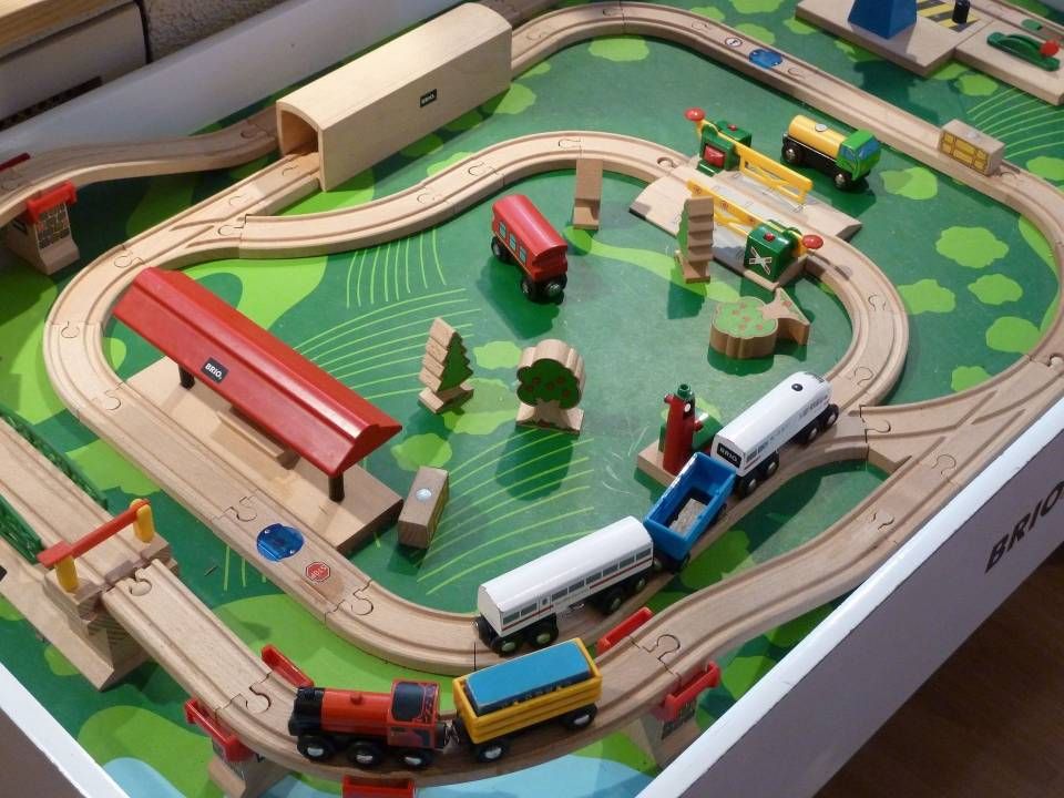 Circuit de train miniature sur table avec trains colorés, bâtiments et aire de jeu verte