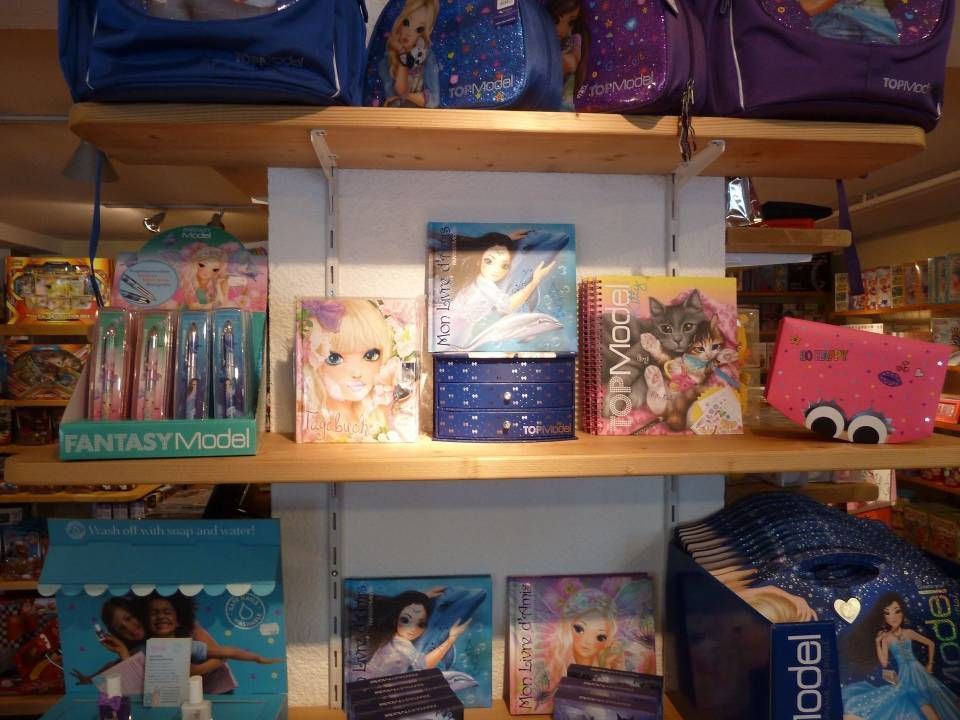 Rayon du magasin avec des boîtes à jouets colorées et des coffrets cadeaux, y compris des articles et des sacs sur le thème de Barbie sur l'étagère supérieure