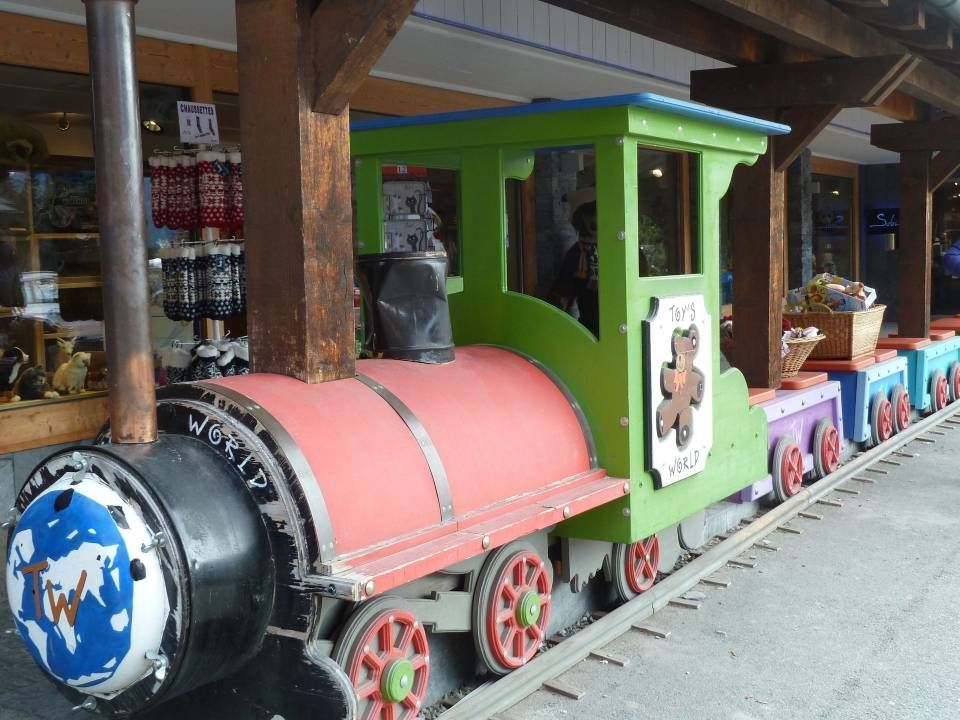 Promenade en petit train coloré avec une locomotive bleue, des wagons rouges et une cabine verte dans une gare intérieure