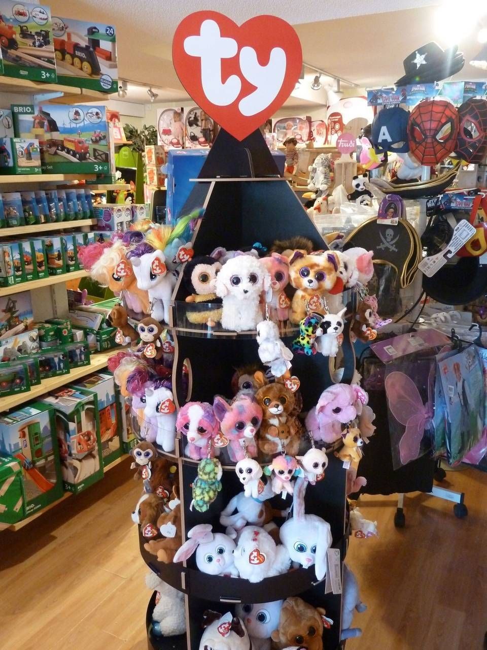 Présentoir de peluches Ty Beanie Babies dans un magasin de jouets, avec des peluches colorées et un logo Ty rouge.