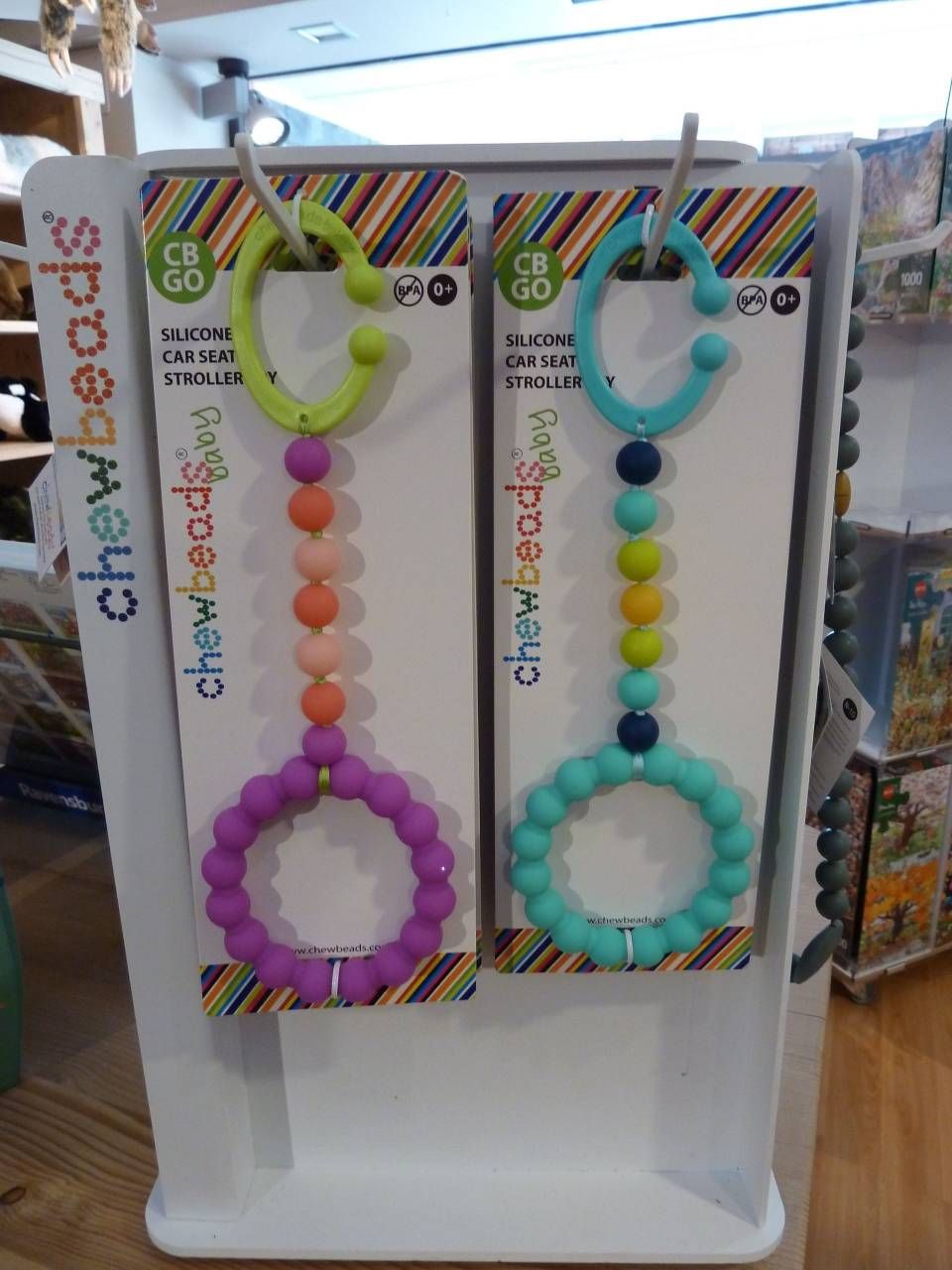 Des colliers de perles colorées, présentés sur un présentoir blanc, avec des cartes arc-en-ciel en arrière-plan.