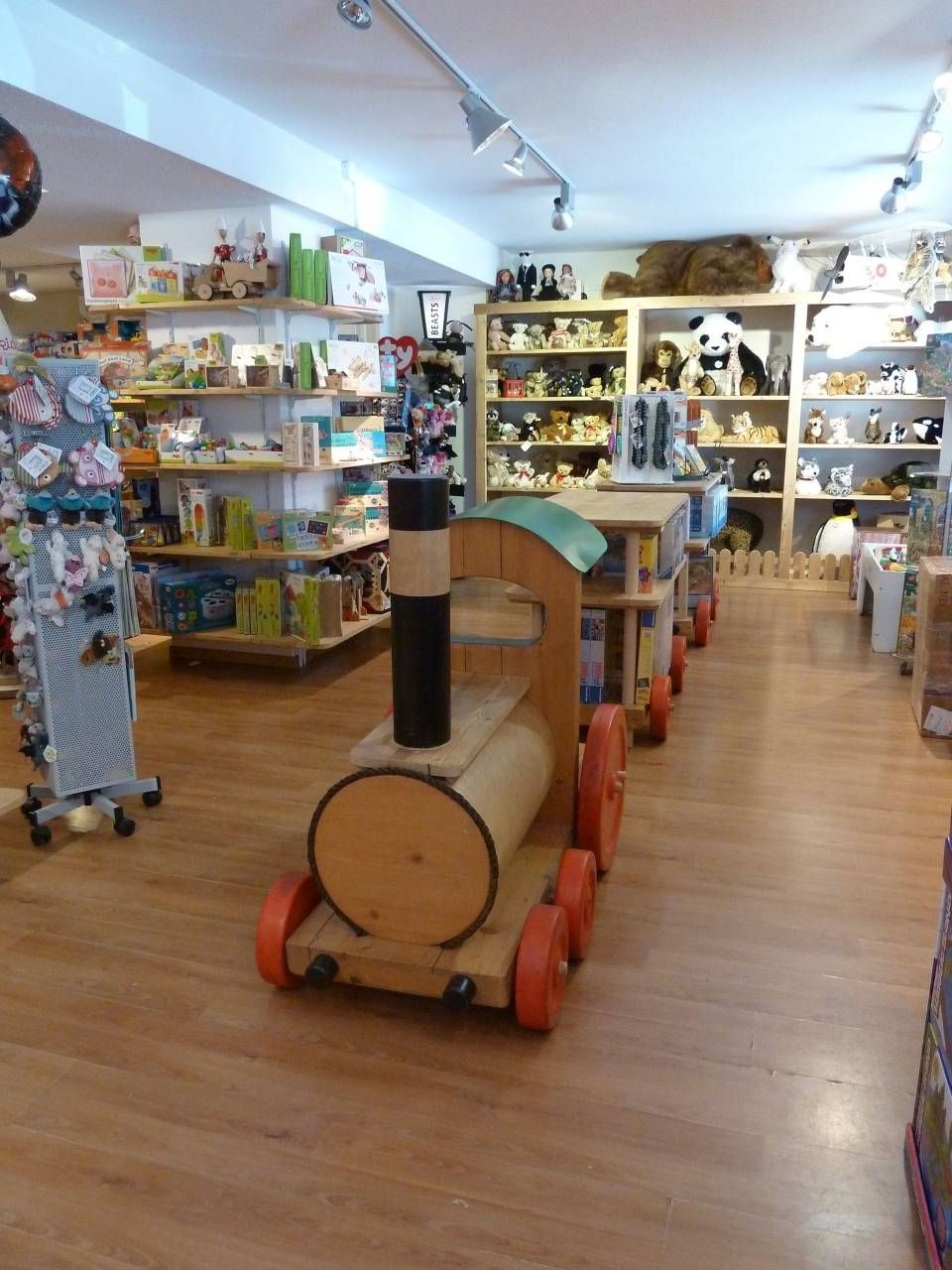 Allée d'un magasin de jouets avec un train miniature en bois au premier plan et des étagères de jouets le long des murs.