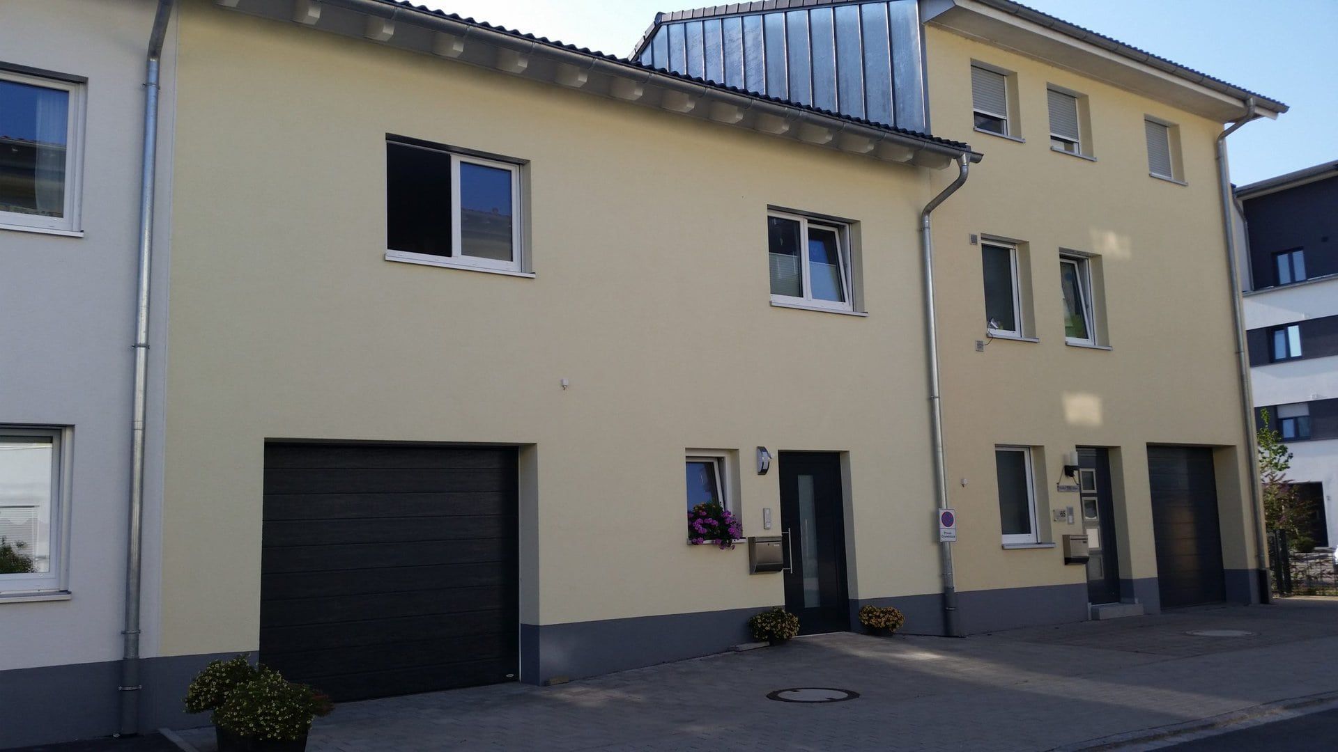 Gelbes zweistöckiges Gebäude mit Garage, Fenstern und dunkler Tür an einer Straße.