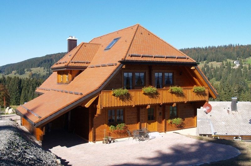 Holzhütte mit rotem Ziegeldach, Blumenkästen und Bergkulisse unter blauem Himmel.