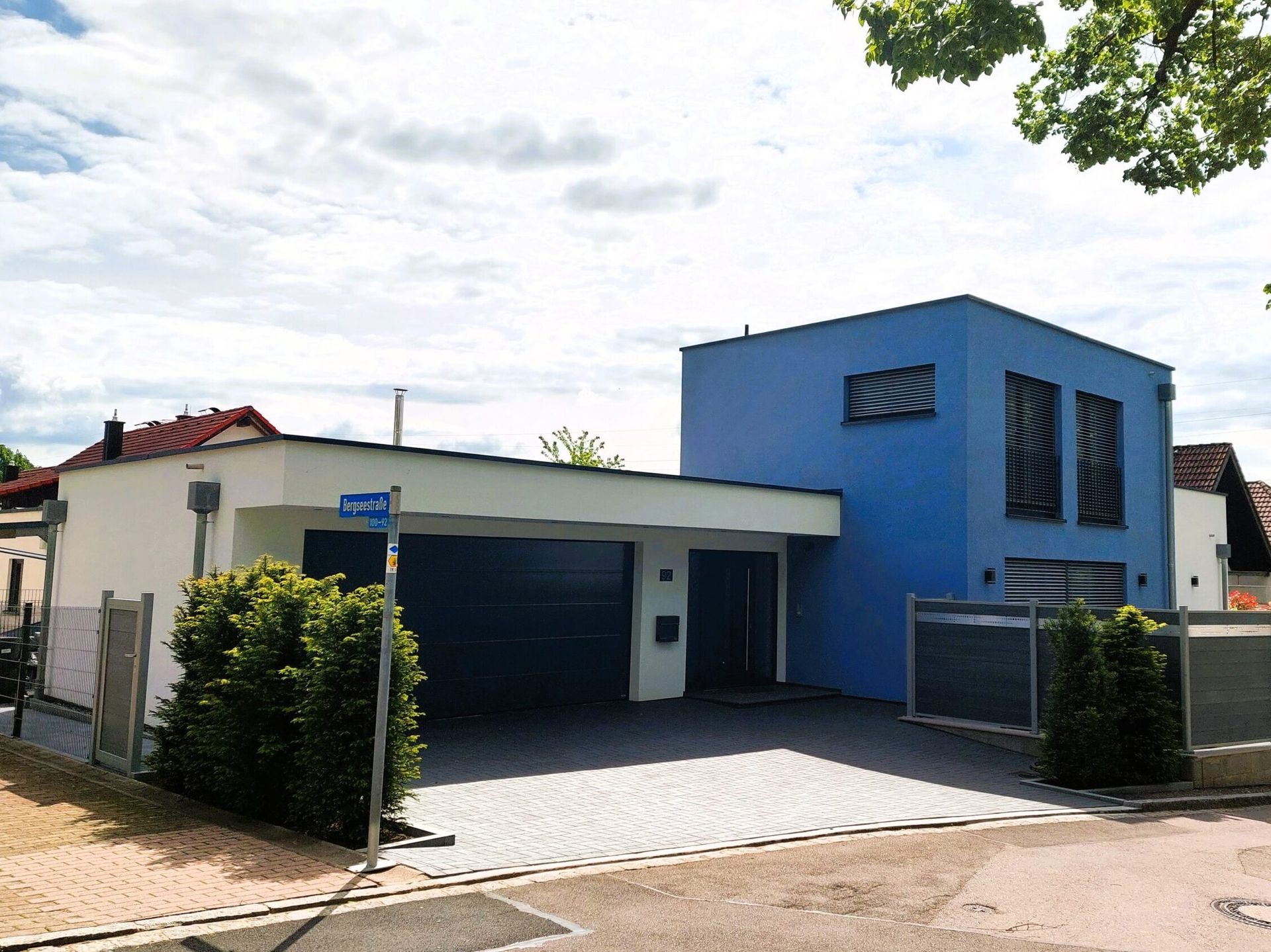 Modernes blau-weißes Haus mit Garage und Einfahrt unter bewölktem Himmel.
