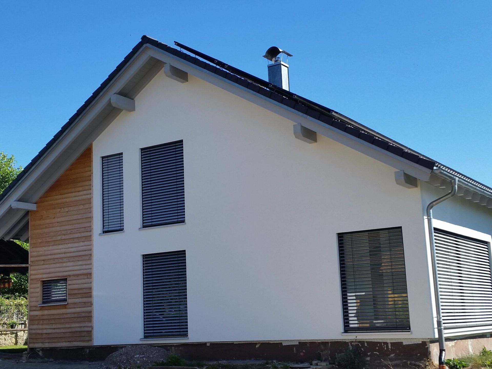 Modernes Haus mit weißen Wänden, Holzverkleidung und schwarzen Jalousien unter blauem Himmel.