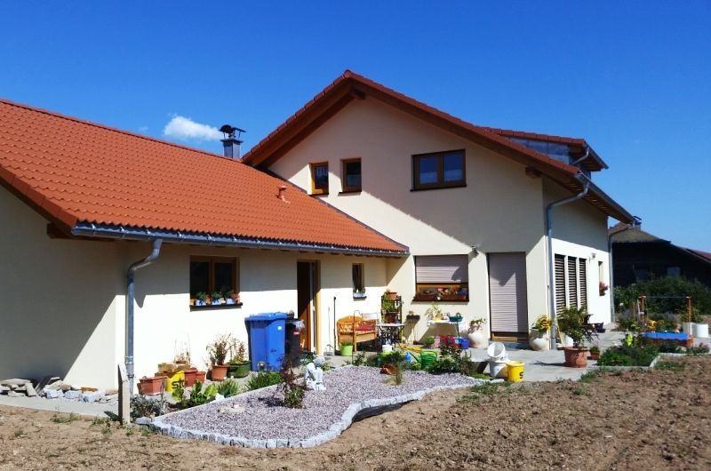 Ein zweistöckiges Haus mit rotem Ziegeldach neben einem kleineren Gebäude; der Himmel ist blau.