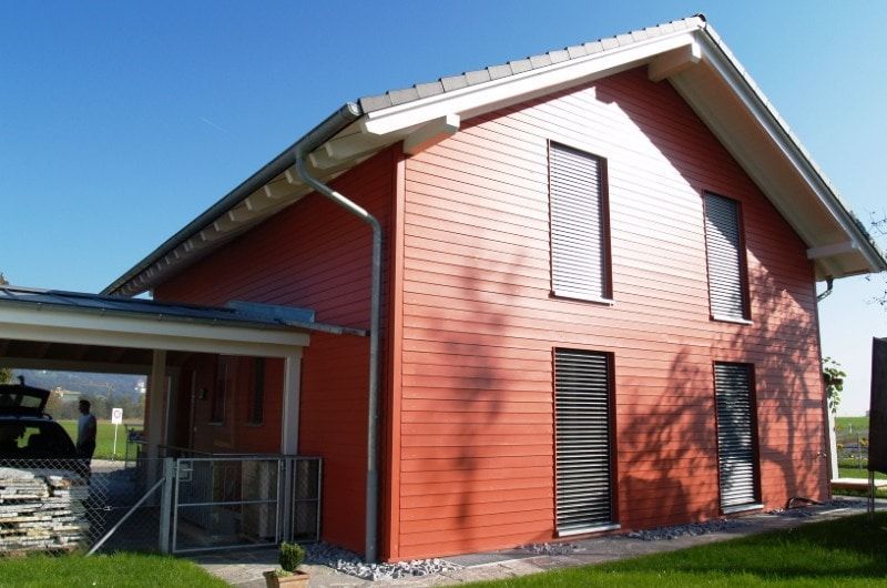Rotes zweistöckiges Haus mit Carport an einem sonnigen Tag.